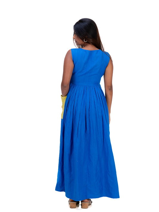 A woman viewed from the back wearing a sleeveless royal Woad Blue maxi dress with a gathered waist and pleated skirt, paired with brown wedge sandals, against a plain white background.