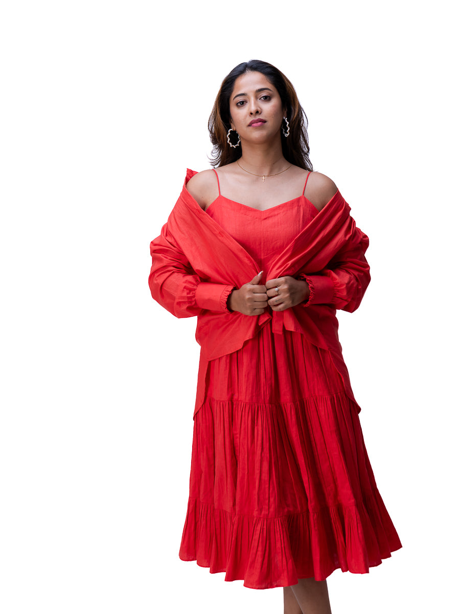 A woman modeling a bright Madder Red tiered midi dress with long sleeves and a matching draped shawl, set against a solid white background.