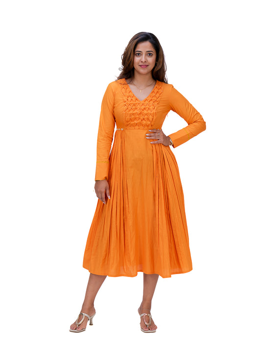 A woman modeling a bright Pomo orange long-sleeve midi dress with a pleated skirt and embroidered bodice, standing against a plain white background.