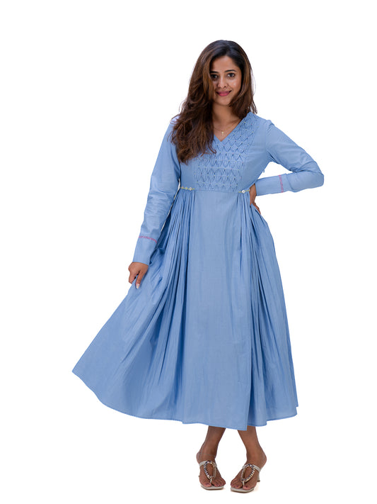 A woman modeling a light Nile Blue long-sleeve maxi dress with a V-neckline and delicate embroidery on the bodice, set against a plain white background.