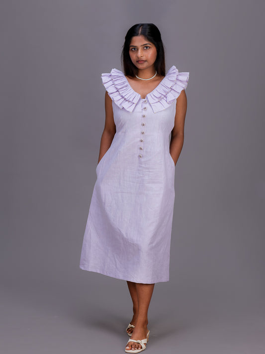 A woman modeling a sleeveless midi dress in a very light lavender or pale Cherry Pink color. The dress features a wide ruffled collar, a button-down front, and side pockets, photographed against a solid gray studio background.