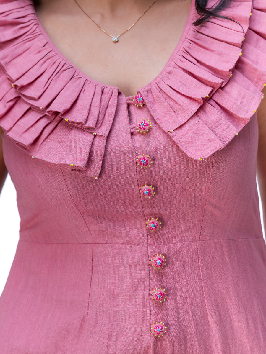 Close-up of a dusty Ash pink dress featuring a large layered ruffle collar and decorative pink and gold buttons down the front center.