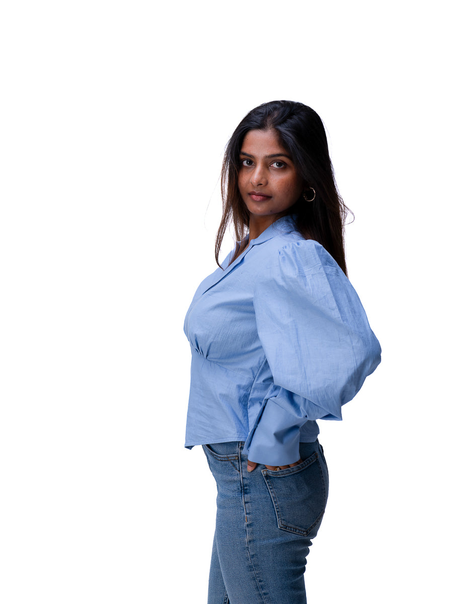 A woman wearing a Nile Blue long-sleeve button-up blouse with puffed shoulders and blue jeans, standing against a plain white background.