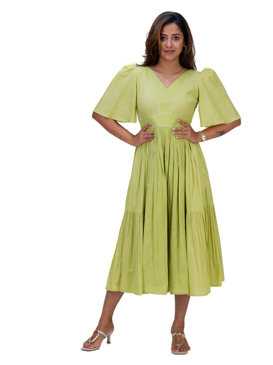 A woman modeling a light lime Dahlia Green midi dress with puff sleeves, a V-neckline, and a tiered skirt, set against a plain white background.