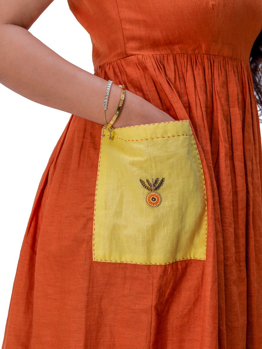 Close-up of a woman wearing an Mud Orange dress with a large yellow patch pocket featuring a small embroidered motif on the front.