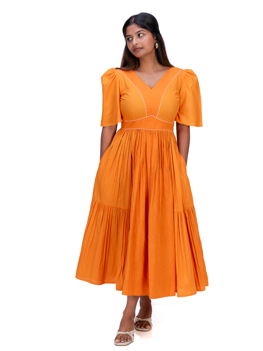 A woman modeling a bright Pomo orange midi dress with puff sleeves, a V-neckline, and a pleated tiered skirt against a plain white background.