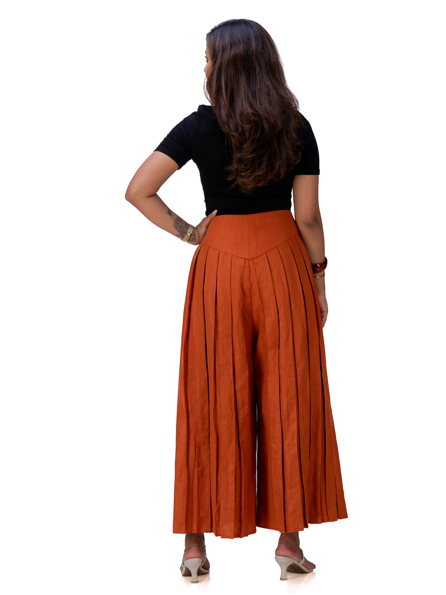 A woman shown from the back wearing a black short-sleeve top and a high-waisted, wide-leg pleated skirt in Brazil Brown, paired with beige heels, against a plain white background.