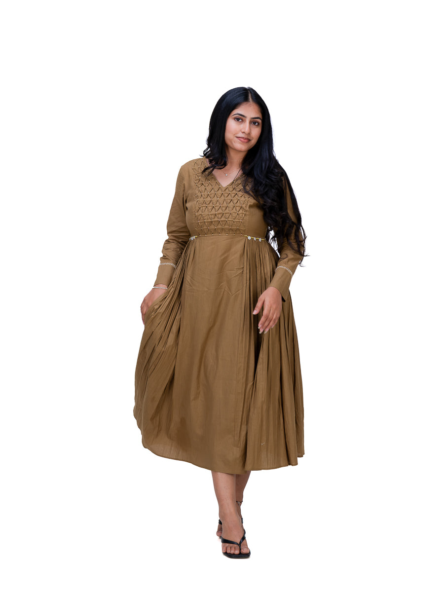 A woman modeling a long-sleeved Oak Brown maxi dress with embroidered detailing on the bodice and a pleated skirt, set against a plain white background.