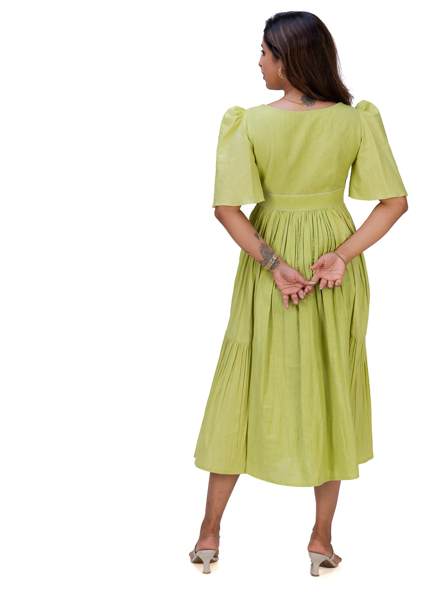 A woman wearing a light lime Dahlia Green midi dress with puff sleeves and a tiered skirt, shown from the back against a plain white background.