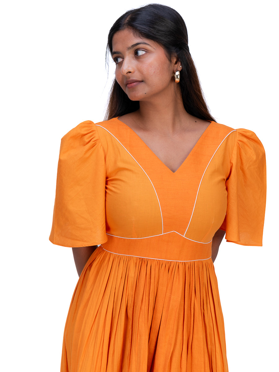 A woman wearing a bright Pomo orange dress with puff sleeves, a V-neckline, and white contrast stitching, shown against a plain white background.