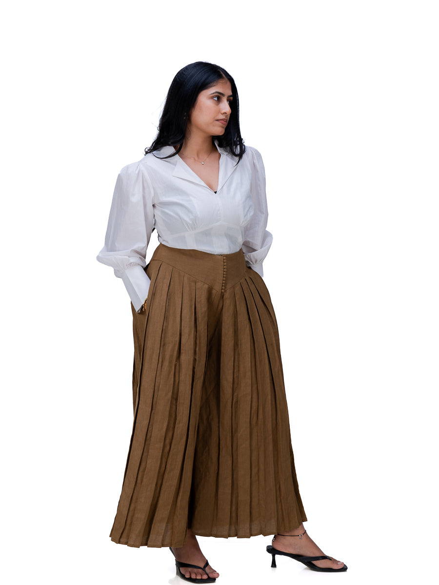 A woman modeling a white long-sleeve blouse and a high-waisted, wide-leg Oak Brown pleated skirt, standing against a solid white background.
