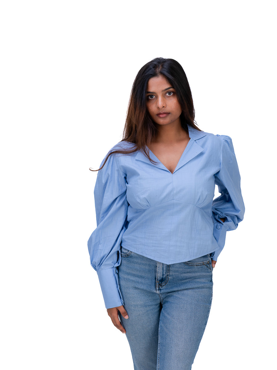 A woman modeling a Nile Blue long-sleeve blouse with puffed balloon sleeves and a V-neckline, paired with blue jeans, against a solid white background.