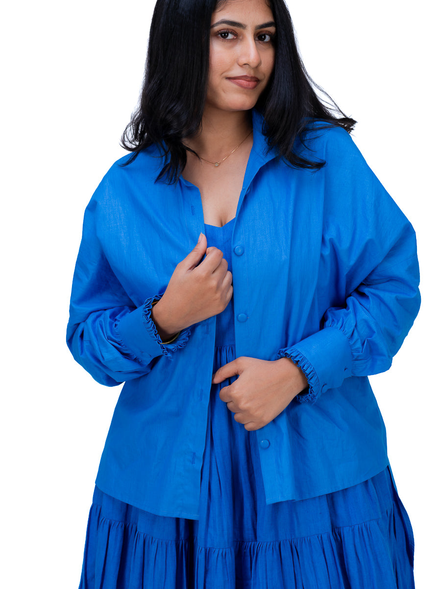 A woman wearing a bright royal Woad Blue  long-sleeve button-up shirt and matching tiered skirt, shown against a plain white background.