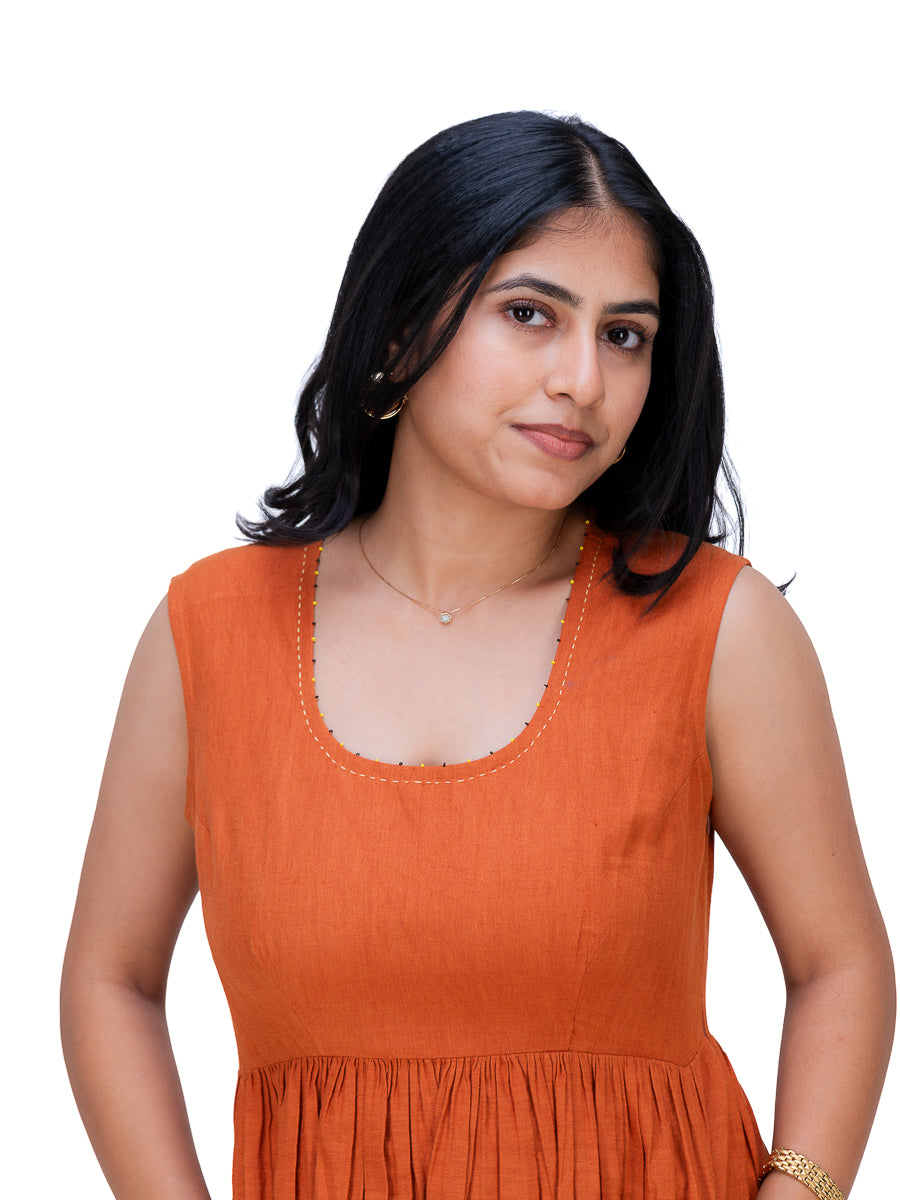 A woman with black hair wearing a sleeveless burnt Mud Orange dress, photographed against a solid white background.