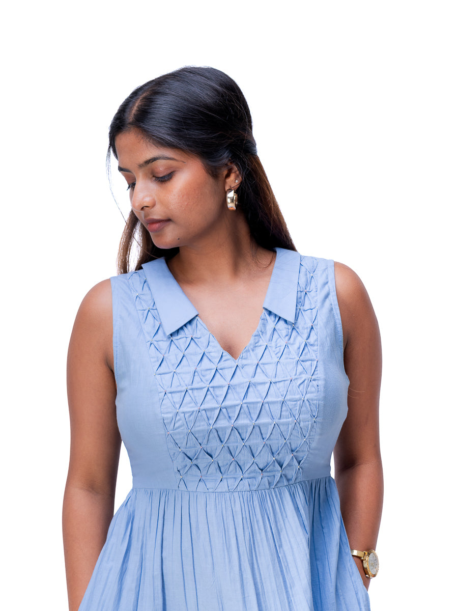 A woman wearing a Nile Blue sleeveless dress with a textured geometric pattern on the bodice and a pleated skirt, shown against a plain white background.