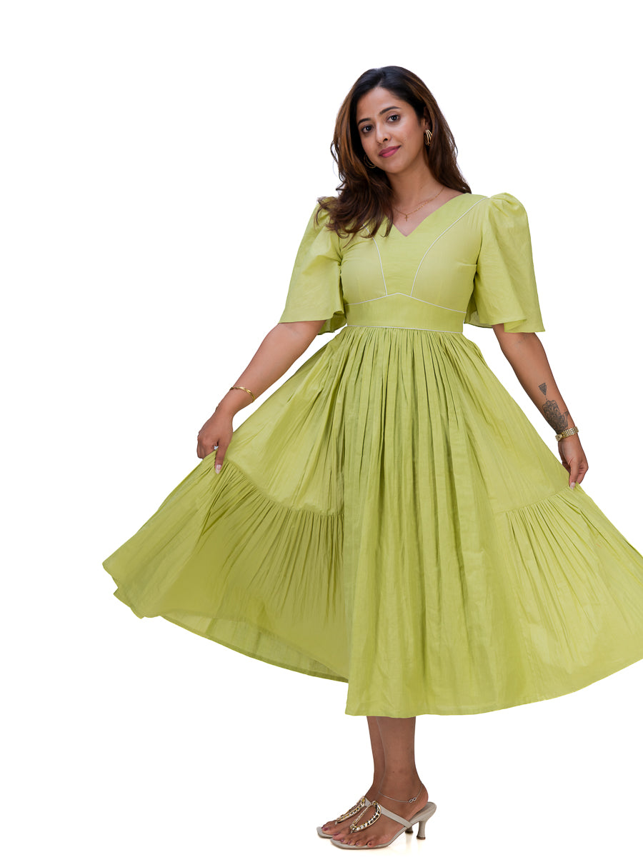 A woman modeling a light lime Dahlia Green midi dress with short puff sleeves, a V-neckline, and a tiered pleated skirt, shown against a plain white background.
