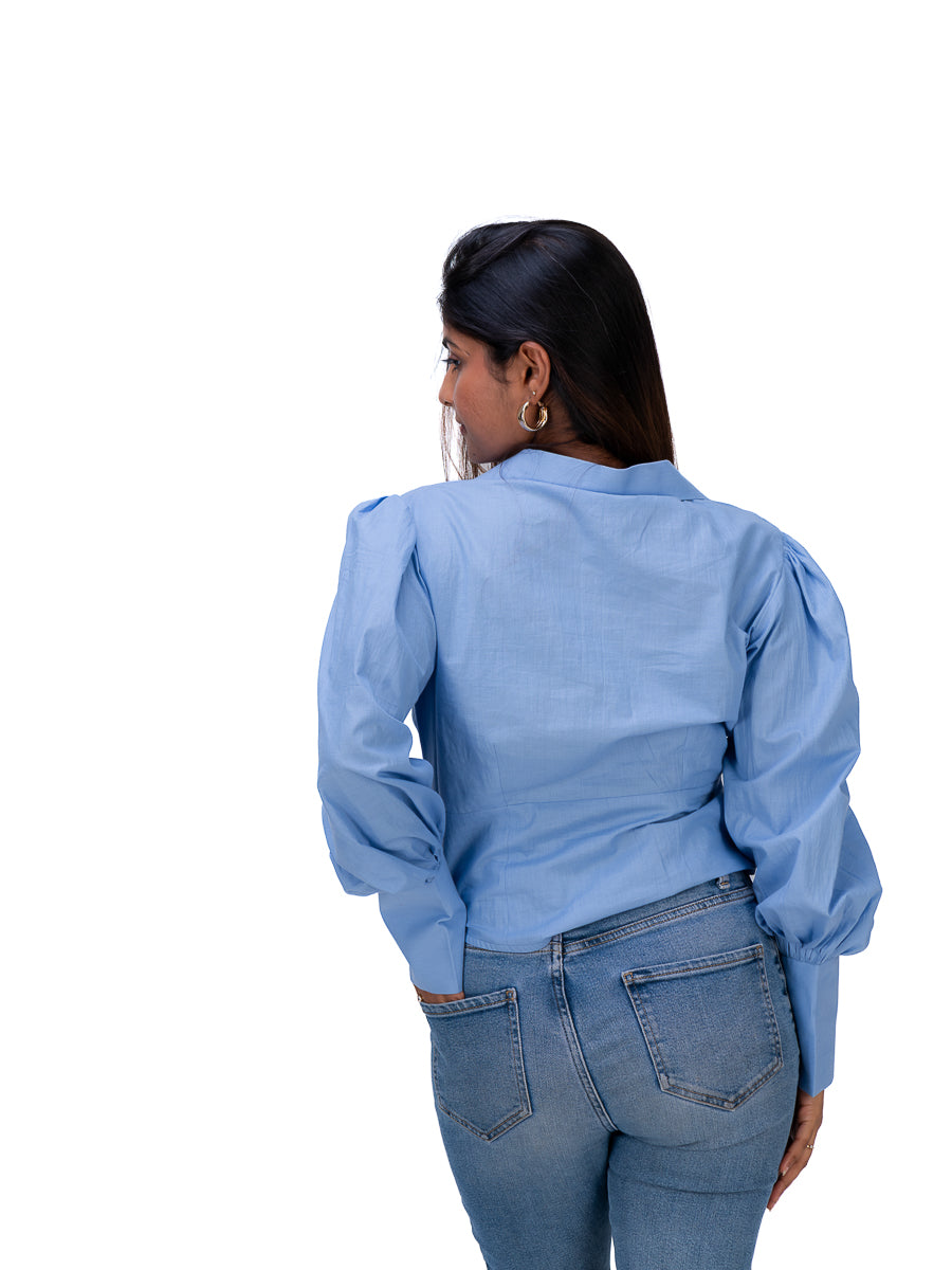 A woman shown from the back wearing a Nile Blue long-sleeve blouse with puffed shoulders and blue jeans, photographed against a plain white background.