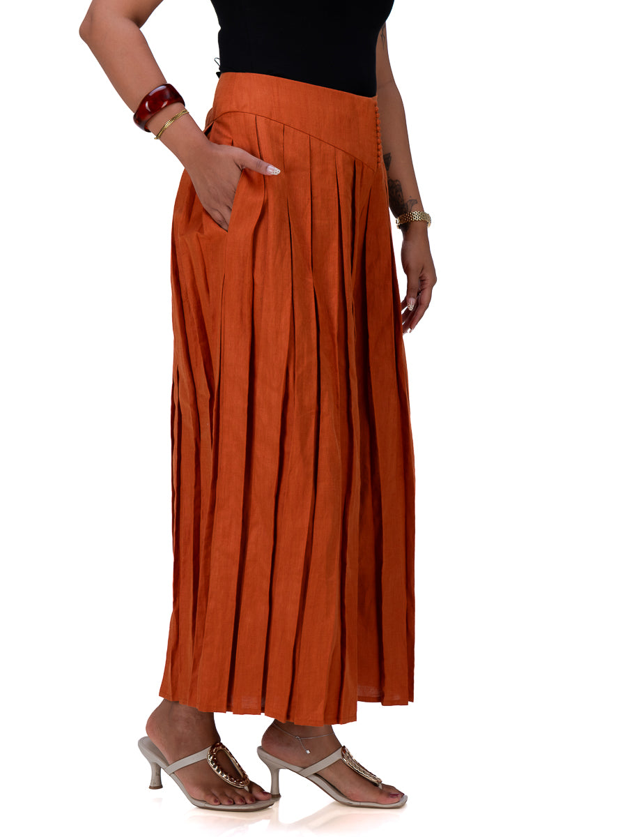 A woman wearing a Brazil Brown pleated maxi skirt with side pockets, paired with a black top and beige heeled sandals, shown from the waist down against a white background.