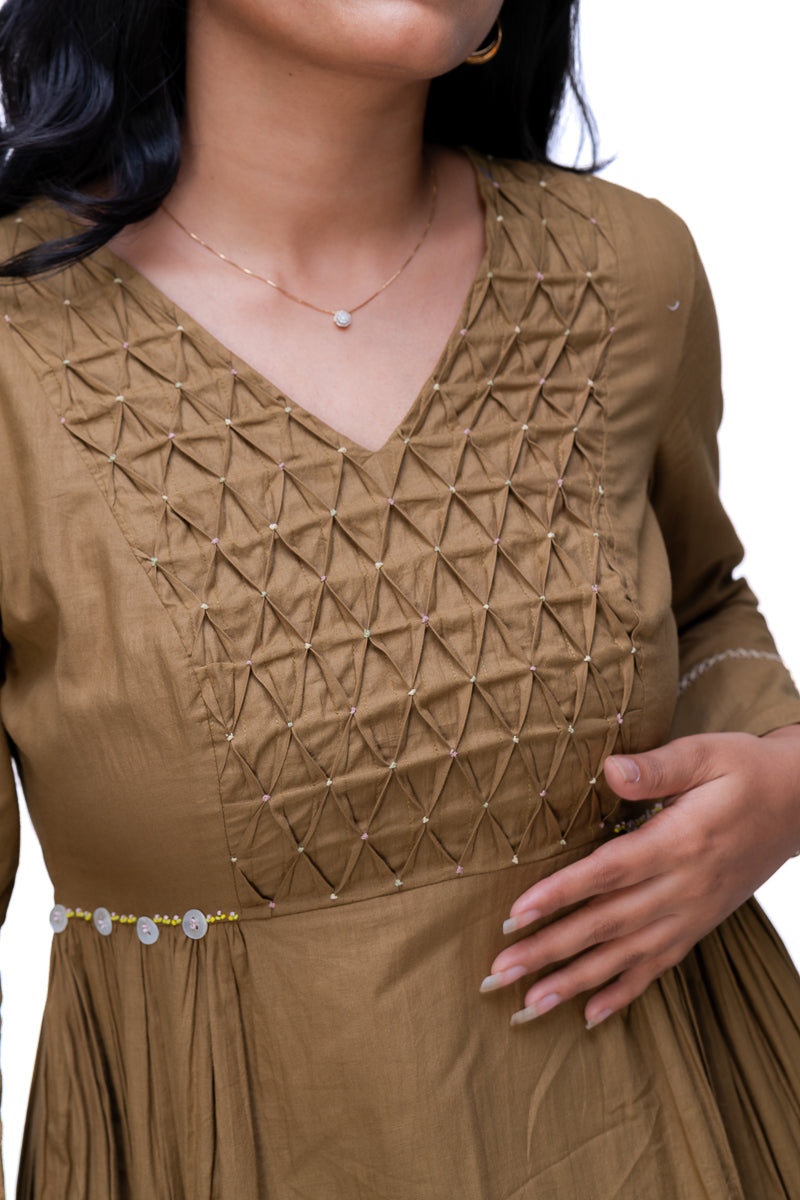 A close-up of a woman wearing a Oak Brown long-sleeve dress with geometric embroidered detailing on the bodice and a beaded waistband, shown against a plain white background.