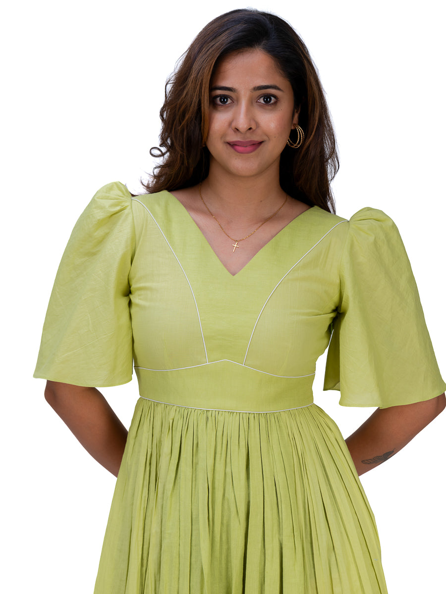 A woman wearing a light lime Dahlia Green dress with puff sleeves, a V-neckline, and a pleated skirt, shown against a plain white background.