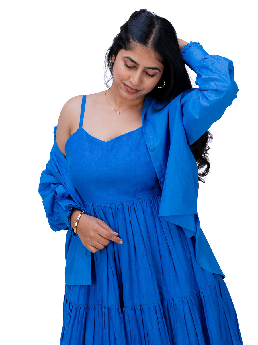 A woman wearing a bright royal Woad Blue  tiered dress with spaghetti straps and a matching oversized long-sleeve jacket, posed against a solid white background.