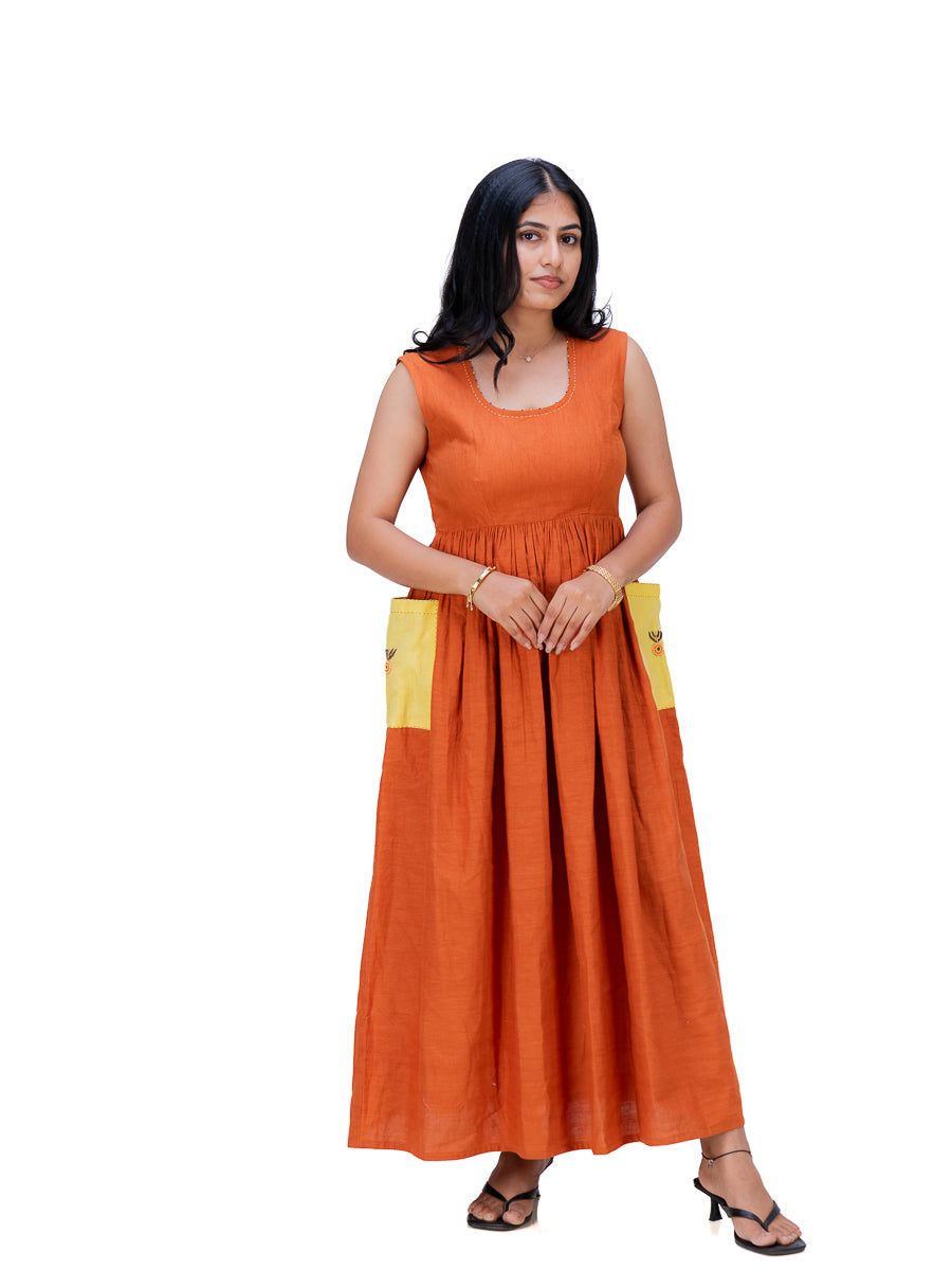 A woman modeling a sleeveless Mud Orange maxi dress with yellow pocket details on the sides, standing against a plain white background.
