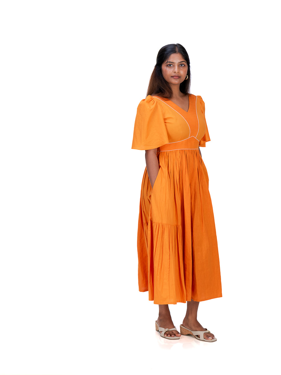 A woman modeling a bright Pomo orange midi dress with short puff sleeves, a V-neckline, and side pockets, standing against a plain white background.