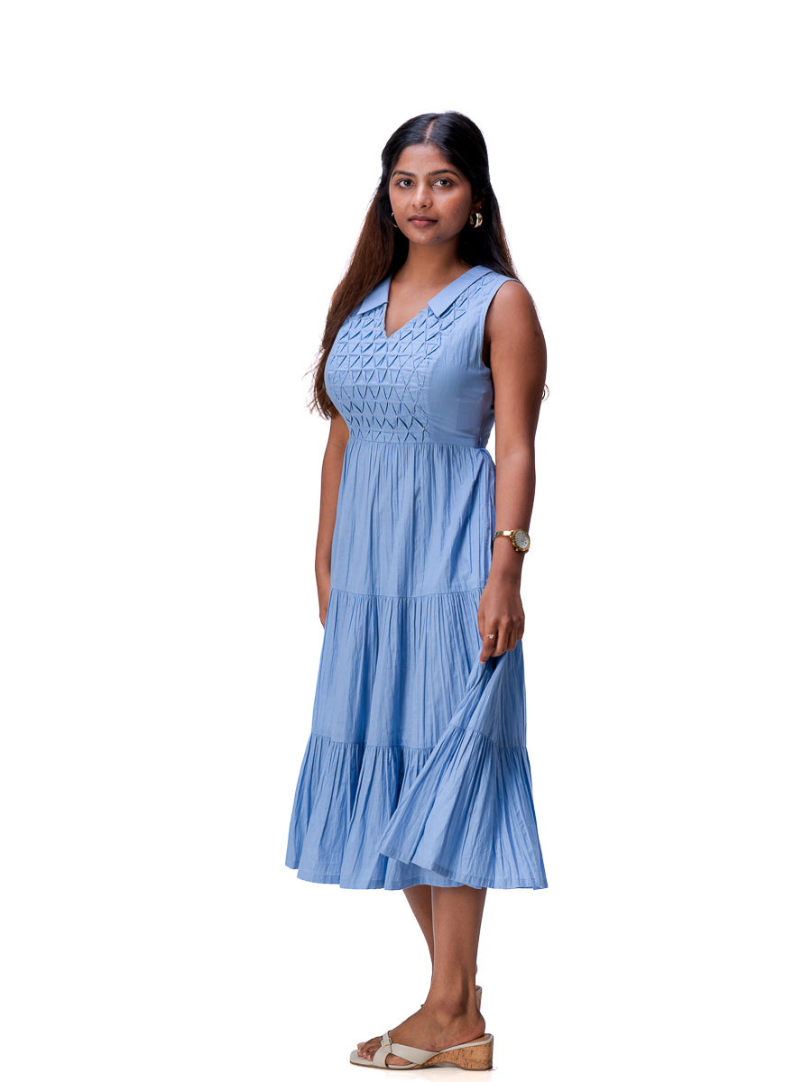A woman modeling a sleeveless Nile Blue tiered midi dress with a smocked bodice, standing against a plain white background.