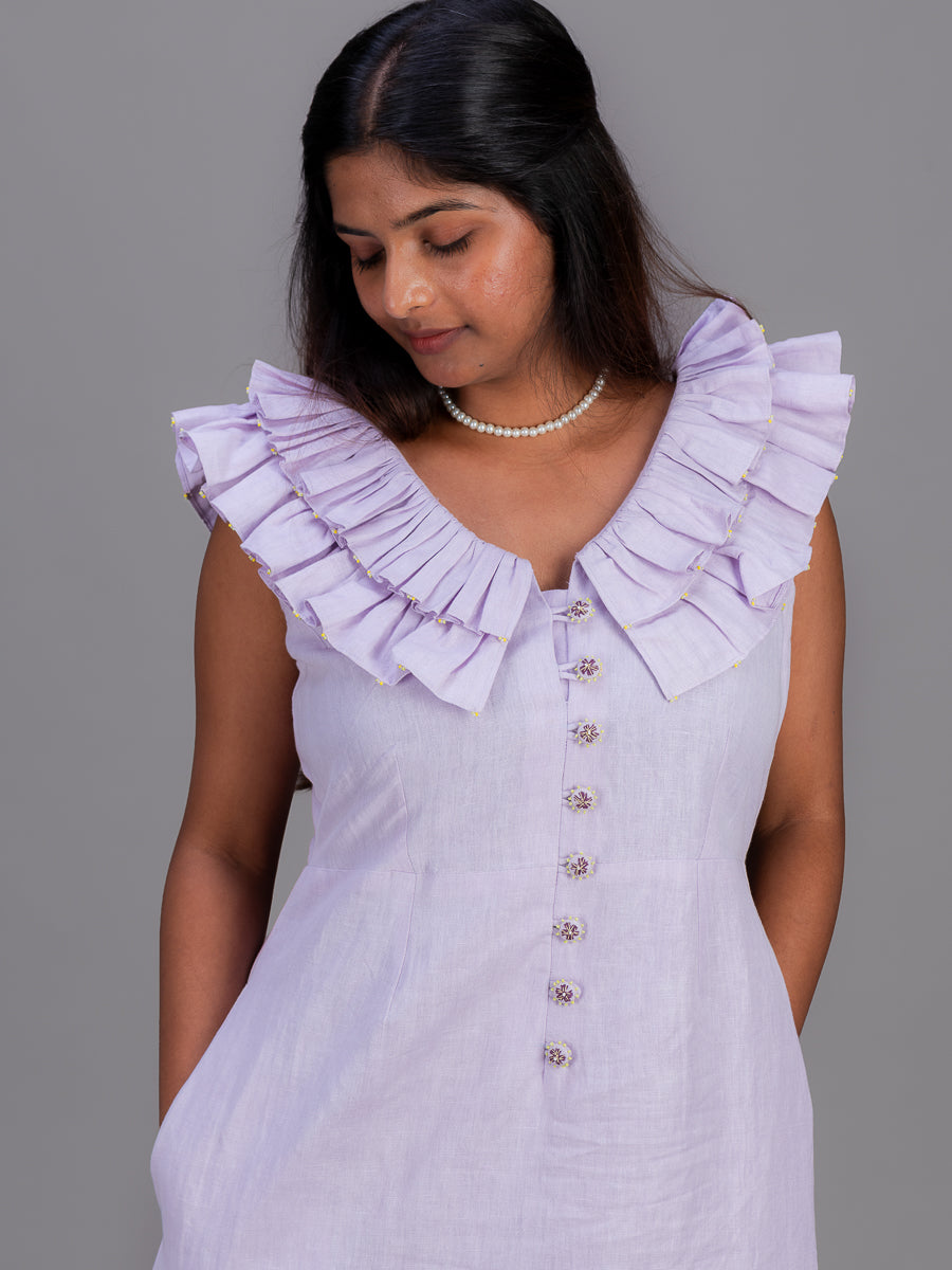 A woman wearing a light Cherry Pink ruffled sleeveless dress with a button-down front, photographed against a solid gray studio background.