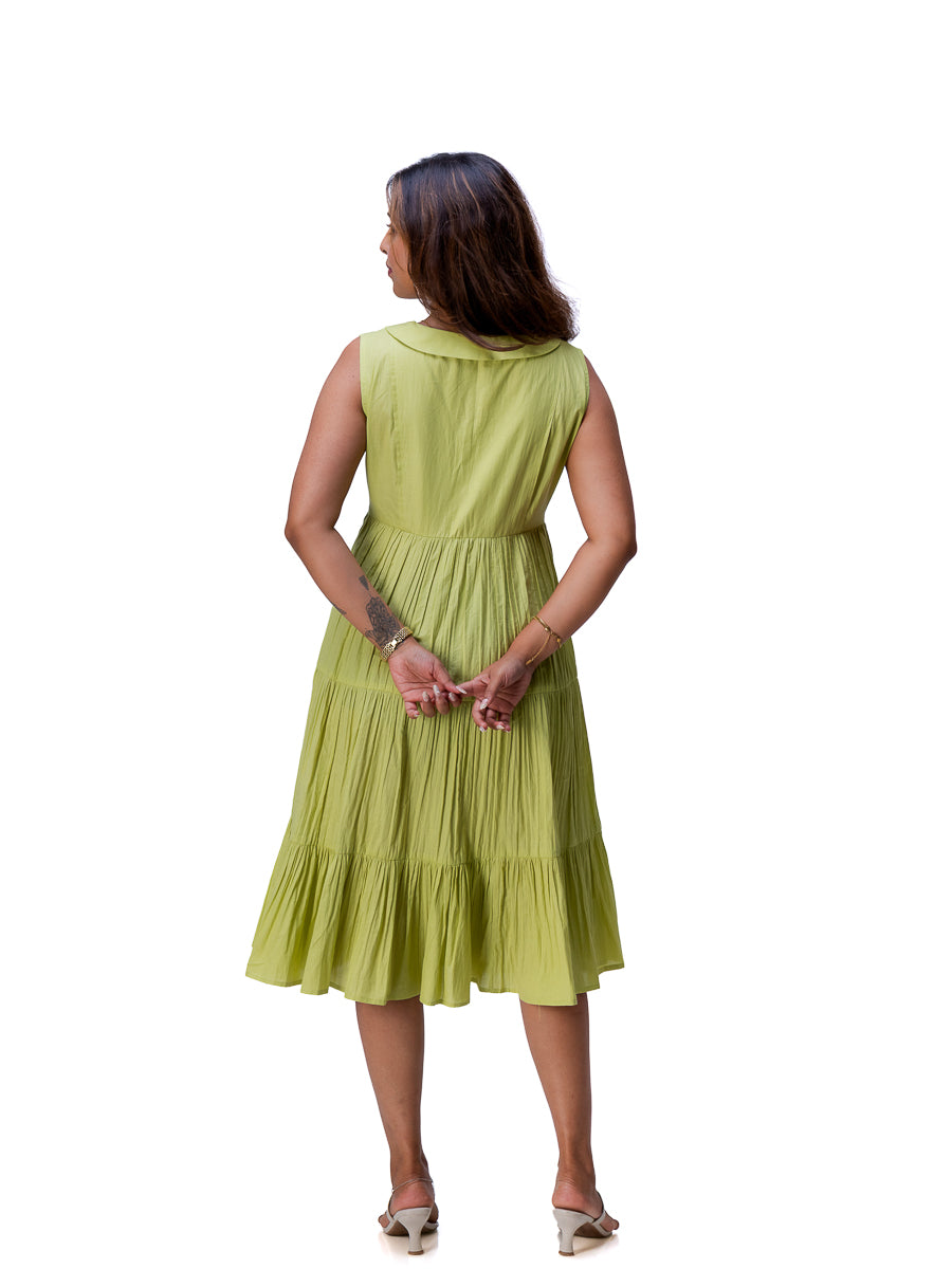 A woman viewed from behind wearing a sleeveless tiered midi dress in a light Dahlia Green color, paired with beige high-heeled sandals, against a plain white background.