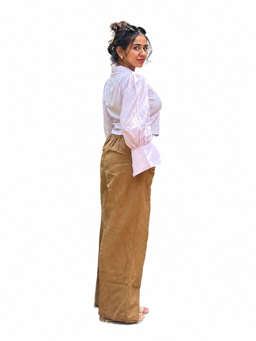 A woman shown in profile wearing a Ash pink long-sleeve blouse with a sheer ruffled sleeve and high-neckline, paired with wide-leg brown pants, against a plain background.